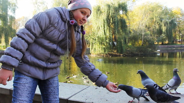 cute teen girl standing feeds pop-corn pigeons from hand