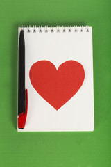 Red heart with a black pen on white notebook