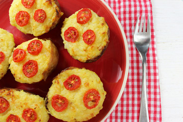 Twice baked potatoes with cheese and tomatoes on a red plate