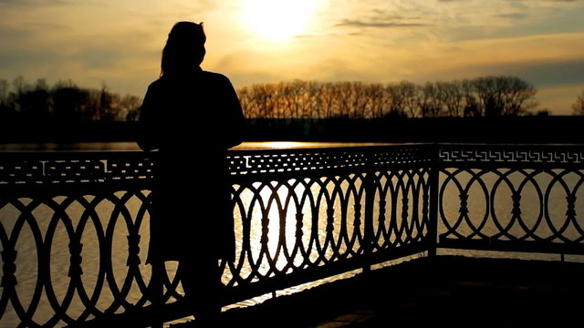silhouette of lady that lean on railings near clear lake, sunset
