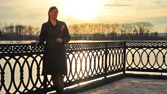 pretty lady with flower that lean on railings near lake, sunset