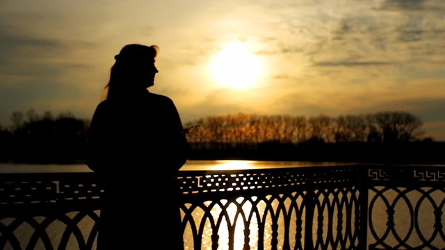 silhouette of lady with flower near clear lake, sunset