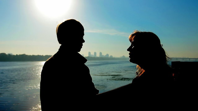 guy with his mother near wide river, silhouette against sunrise