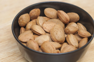 Almonds on a black bowl on wooden background