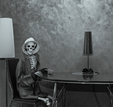 Skeleton sitting behind the table in dark dramatic room