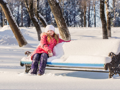little girl sitting on a bench full of snow