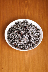 heap of frozen black currant in a plate on the wooden surface