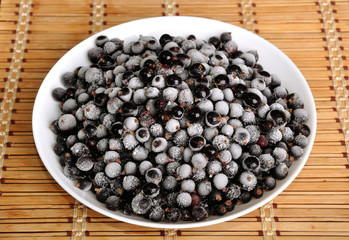 heap of frozen black currant in a plate on the bamboo cloth