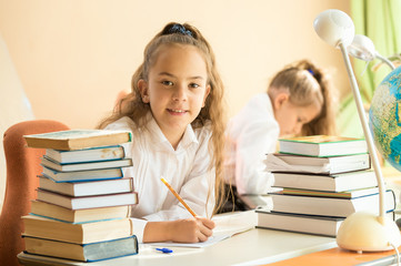 Fototapeta premium smiling girl sitting at school desk and doing homework