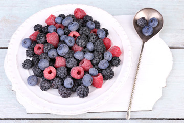 Iced berries on plate, on color wooden background