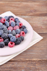 Iced berries on plate, on wooden background