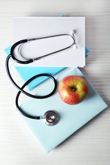 Medical stethoscope with apple on books on wooden table © Africa Studio