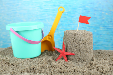 Fototapeta na wymiar Sandcastle with flag and plastic bucket, spade on sandy beach