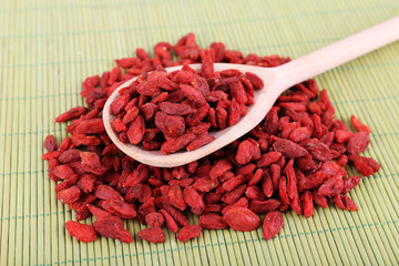 Goji berries in wooden spoon on bamboo mat background