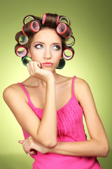 Beautiful girl in hair curlers on green background