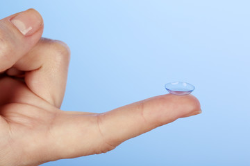 Contact lens on finger on blue background