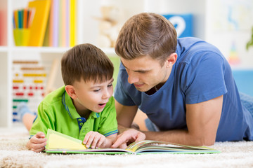 kid boy and his father read a book on floor at home