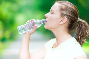 Woman drinking cold mineral water from a bottle after fitness ex