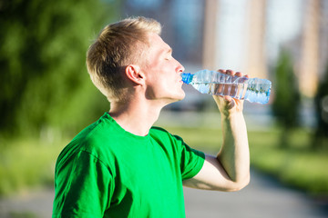 Tired man drinking water from a plastic bottle after fitness