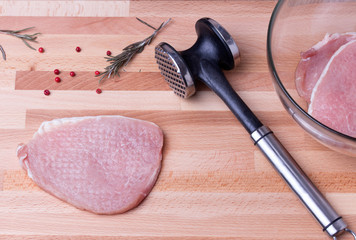 Raw pork schnitzel with meat tenderizer on wooden board