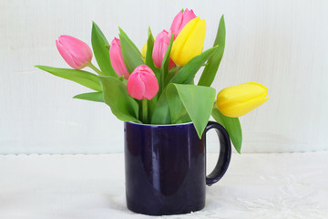 Pink and yellow tulips in navy blue mug