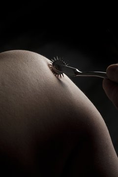 Nude submissive woman shoulder, bdsm act with Wartenberg wheel