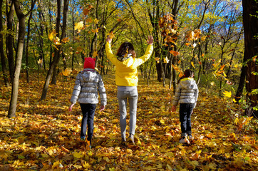 Fototapeta premium Family having fun in autumn forest playing and throwing leaves