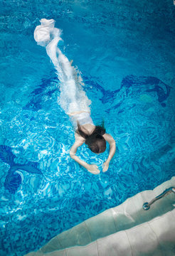 woman in long white dress diving underwater at swimming pool
