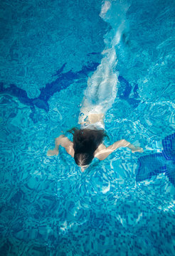 woman covered in long white fabric swimming underwater at pool