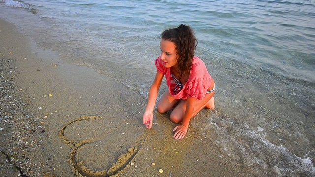 Girl drawing a heart on the beach washed by the waves