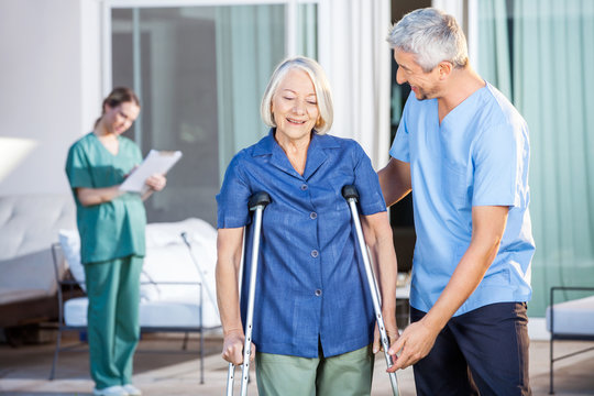 Male Nurse Helping Senior Woman To Use Crutches