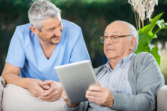 Male Caretaker Looking At Senior Man Using Tablet Computer