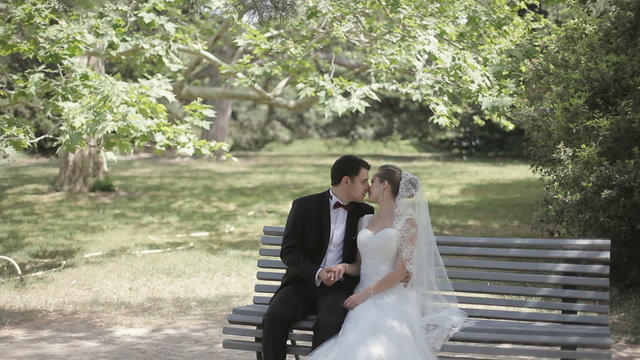 Stylish enamored bride and groom sitting on a bench in the park