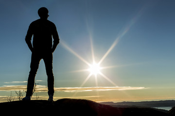 Silhouette male standing on a mountain looking at the sunset
