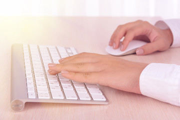 Female hands typing on keyboard on light background