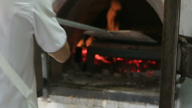 HD Chef putting pizza in a wood fire brick oven