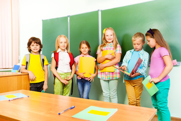 Six children stand in row near blackboard