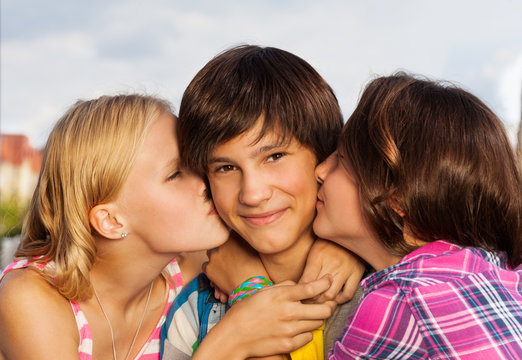 Two girls kiss boy in cheeks close up view