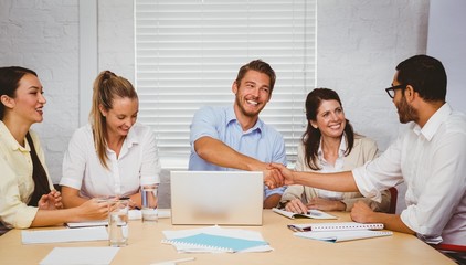Obraz premium Casual business people shaking hands at desk and smiling