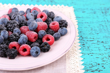 Iced berries on plate, on color wooden background