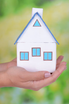 Woman hands holding small house on bright background
