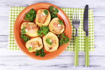 Baked potato with bacon on plate, on wooden background