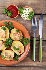 Baked potato with bacon on plate, on wooden background