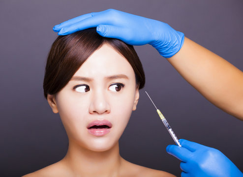 surprised  young woman looking at needle for injection into face