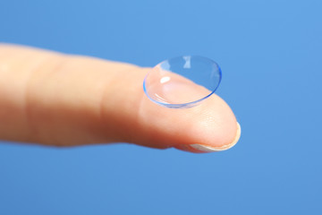 Contact lens on finger on blue background