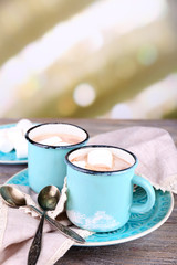 Cups of tasty hot cocoa, on wooden table, on light background