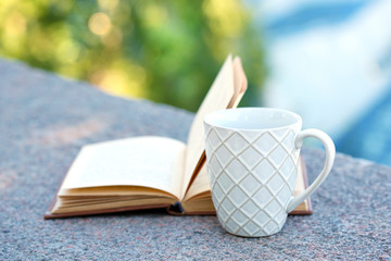 Cup with hot drink and book, outdoors