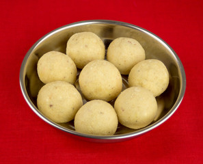Indian laddoo treats in a silver plate against red tablecloth