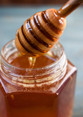 A glass jar with honey and a wooden spoon