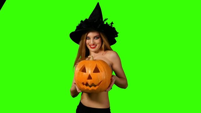 Halloween witch holding a orange pumpkin on green screen.